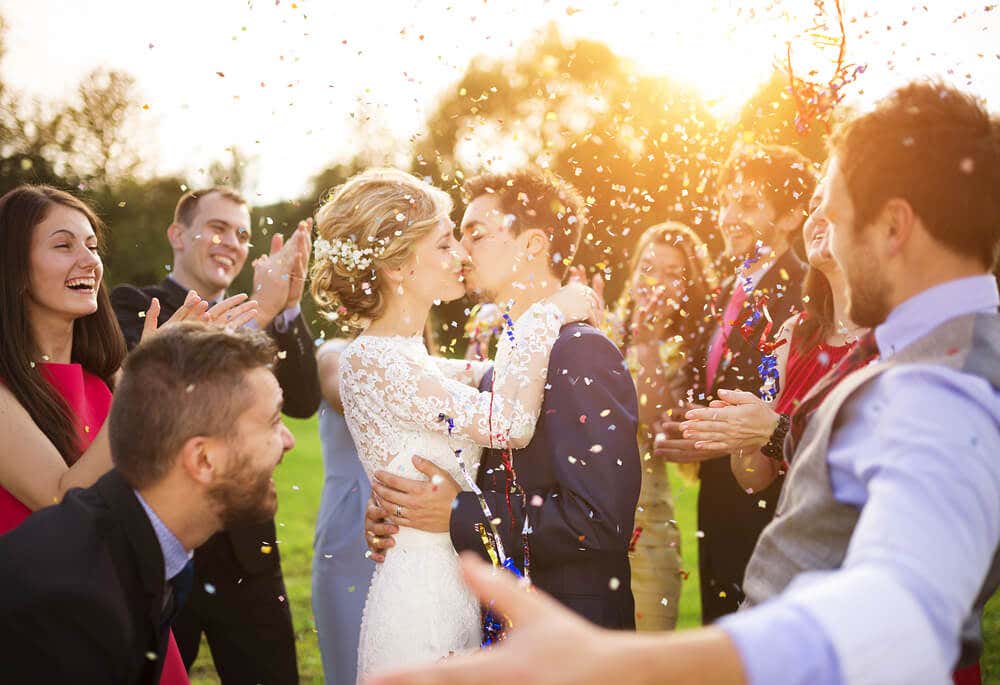 Novio y novia en a boda besándose rodeados de los invitados