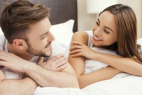 Pareja mirándose y sonriendo encima de la cama