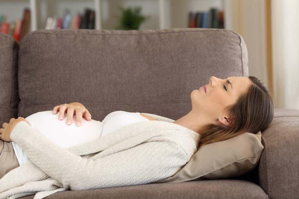 Mujer embaraza tumbada en el sofá con molestias. Típicos cólicos en el embarazo.