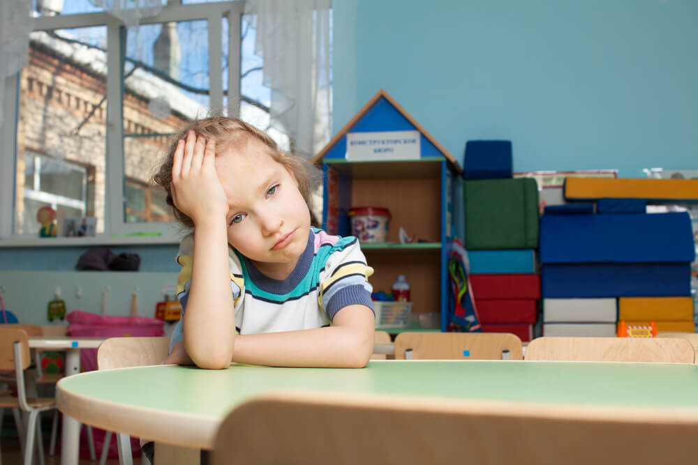 Niña sentada en una mesa del colegio se sujeta la cabeza con expresión triste o frustrada.