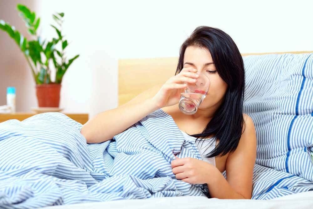 A woman drinking water in bed.