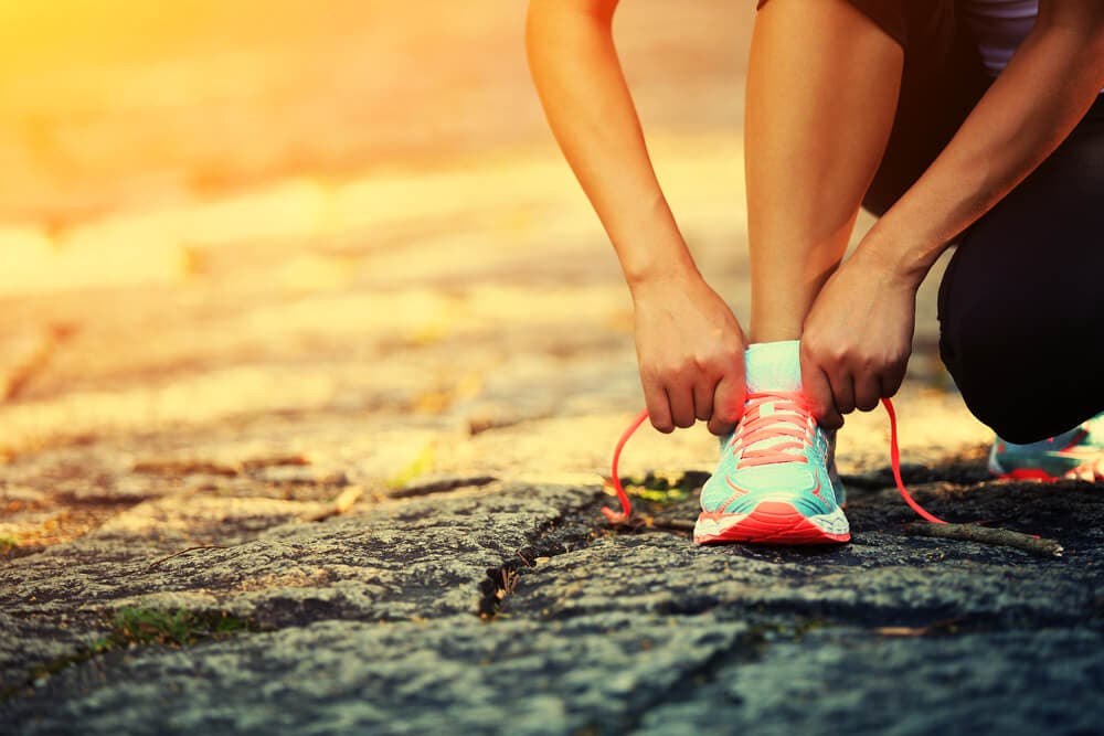 Persona atándose los cordones de la zapatilla deportiva para mantener su peso equilibrado mediante el ejercicio físico