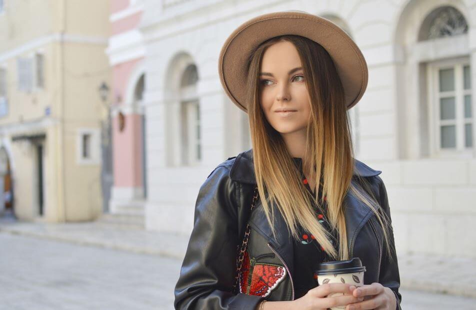 Chica con sombrero tomando café en la calle.