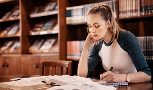Chica joven rubia estudiando en la biblioteca.