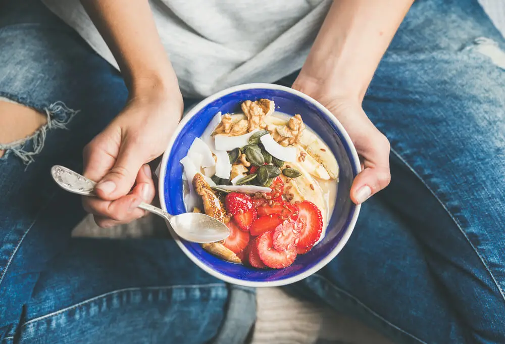 Manos sosteniendo un bol con un desayuno equilibrado: fresas, yogur y frutos secos.