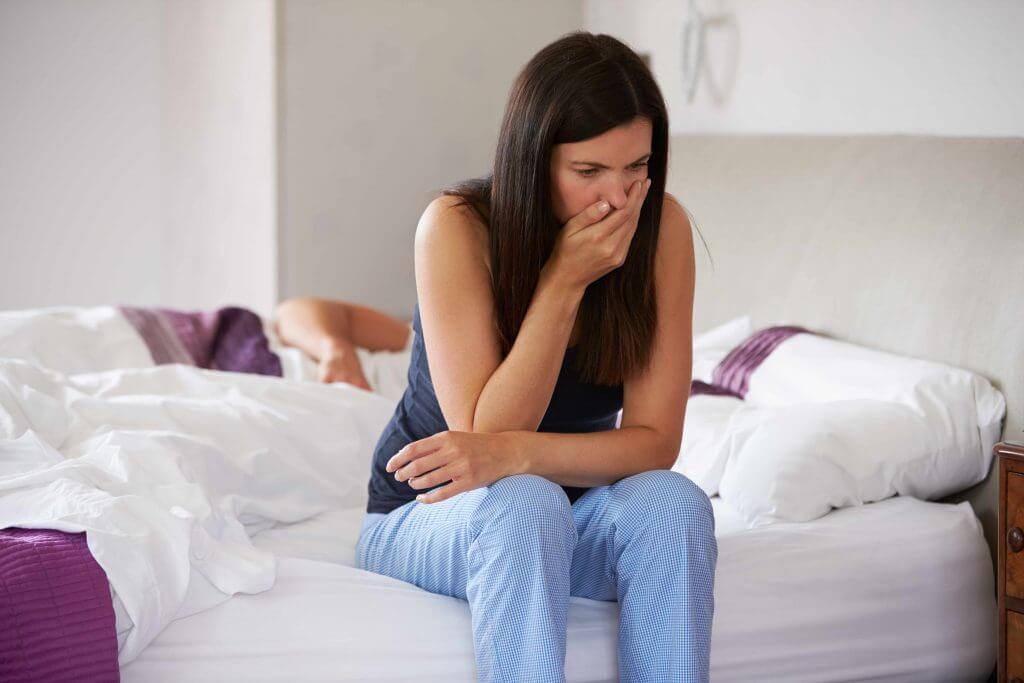 Mujer con náuseas sentada en la cama como consecuencia de un embarazo ectópico
