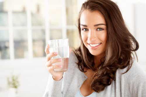 Mujer con vaso de agua en la mano representando consumir agua