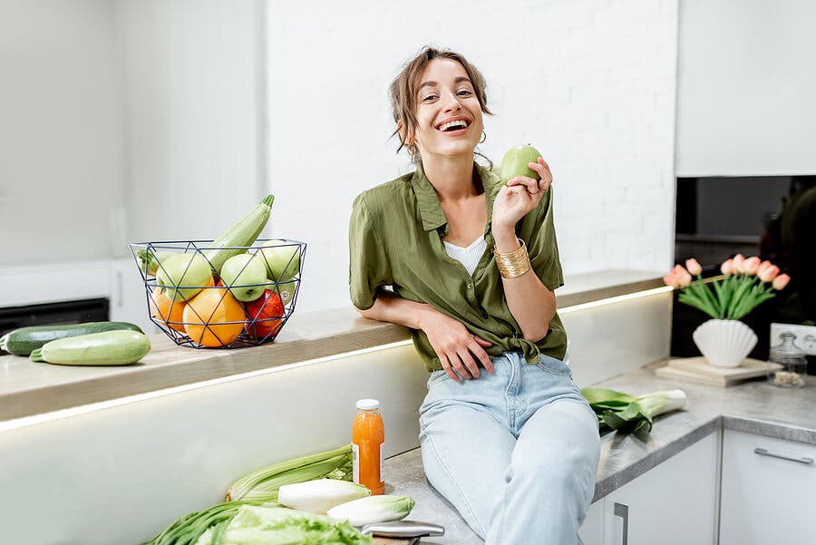 Mujer en la cocina con vegetales alrededor.