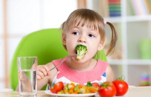 Una niña pequeña come brócoli.