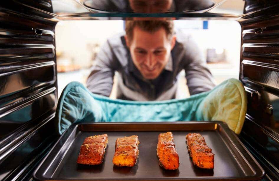 Hombre introduciendo una bandeja con salmón al horno.