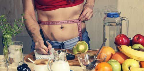 Productos para adelgazar: midiéndose el abdomen y apuntando en una libreta junto con alimentos
