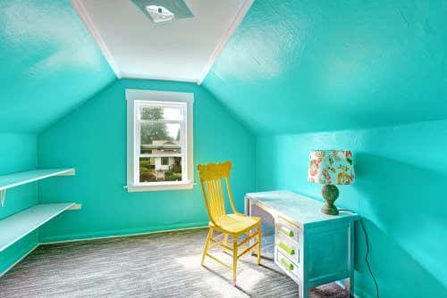 Habitación con paredes de un azul vibrante con un escritorio, una lámpara y una silla amarila