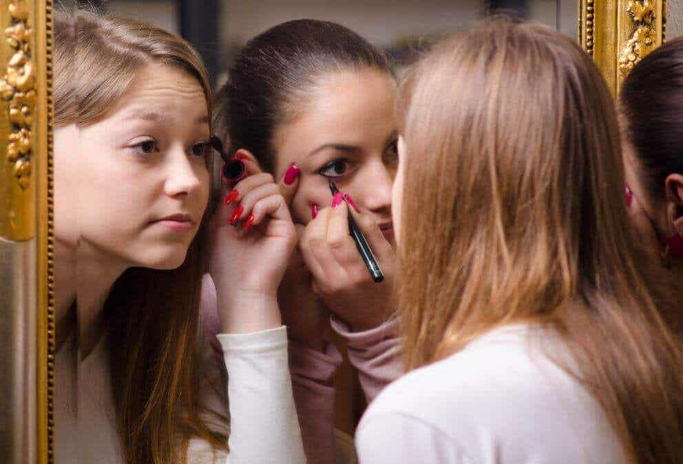Chicas maquillándose los ojos frente a un espejo.