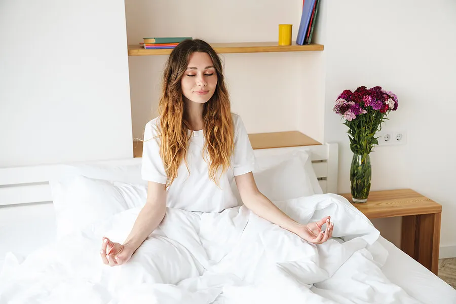 Mujer relajada meditando en su cama.