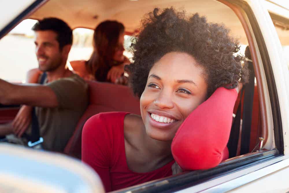 Mujer sonriente apoyada en la ventanilla de un coche yendo de viaje con amigos.
