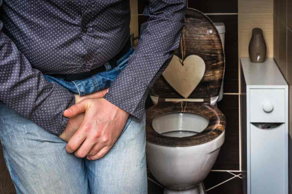 Hombre en el cuarto de baño con las manos en la zona genital: sonda Foley para incontinencia urinaria