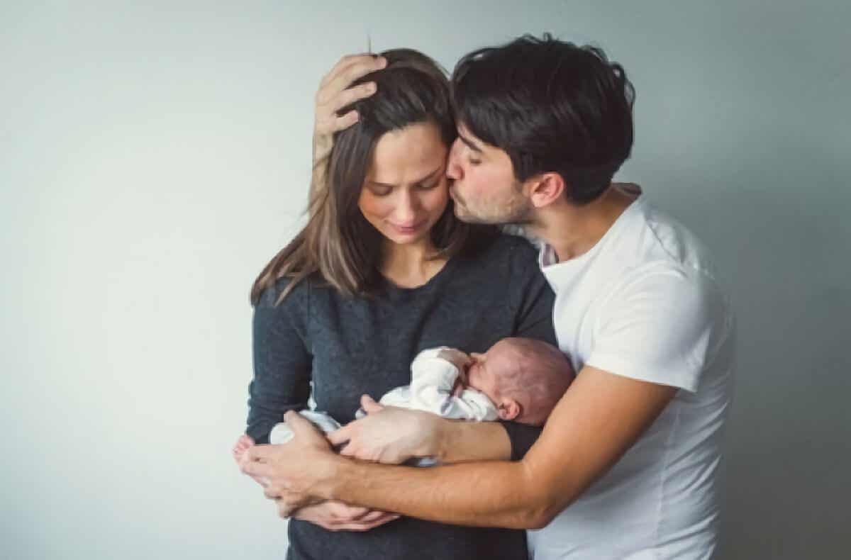 Hombre besando a su pareja que sostiene un bebé