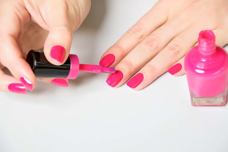 Mujer pintándose las uñas con esmalte rosa.