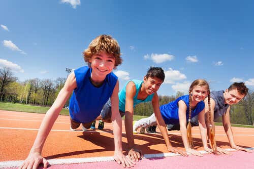 Niños sonríen mientras realizan flexiones en una pista de atletismo.