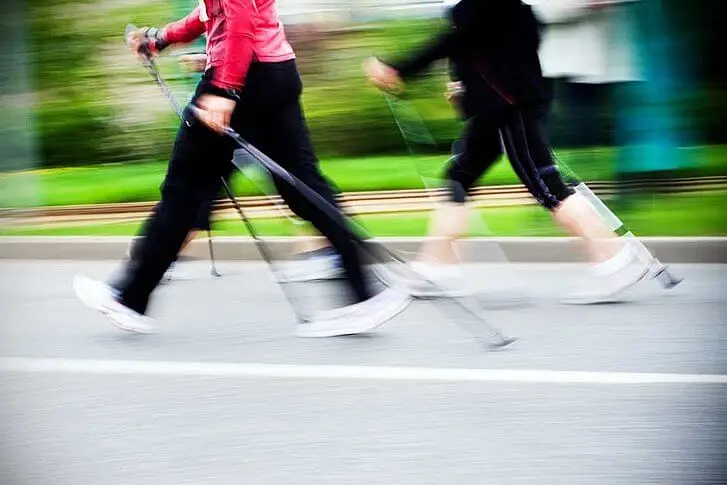 Dos personas en movimiento practican la marcha nórdica por asfalto.