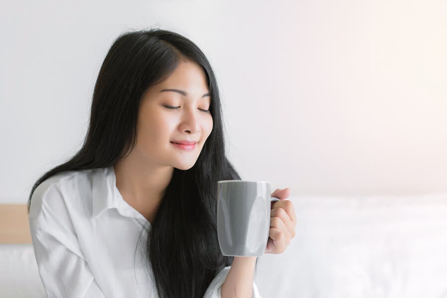 Mujer con los ojos cerrados con taza de té en la cama.