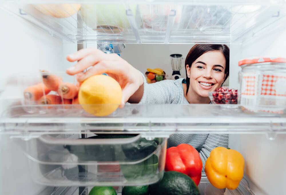 Mujer tomando un limón del refrigerador.