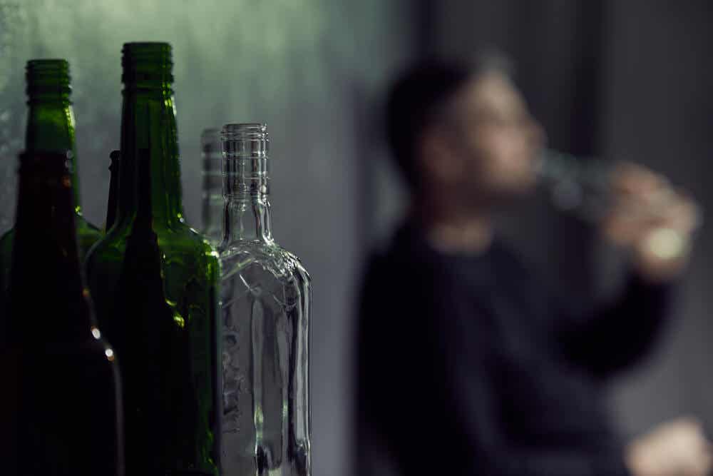 Botellas de vidrio verde y transparente con un hombre al fondo que bebe.