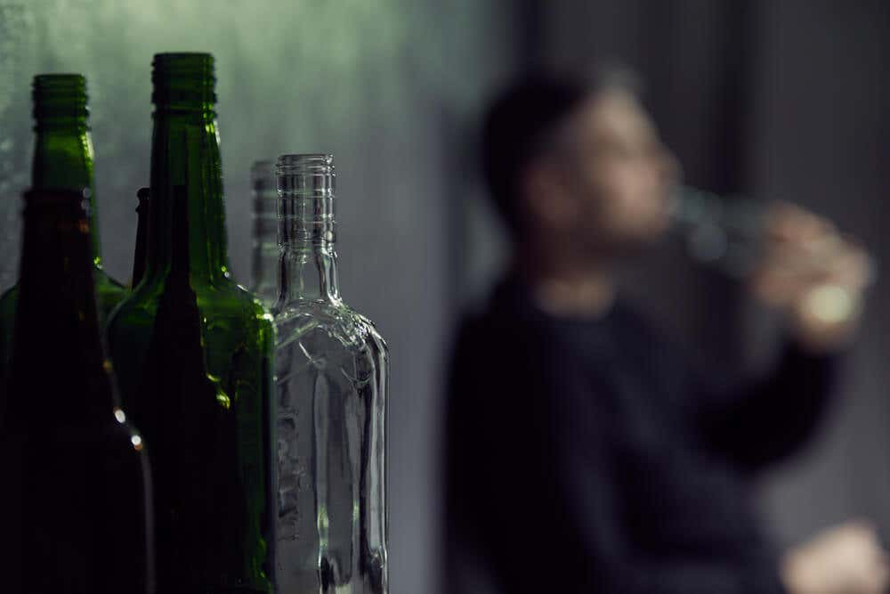 Botellas de vidrio verde y transparente con un hombre al fondo que bebe.