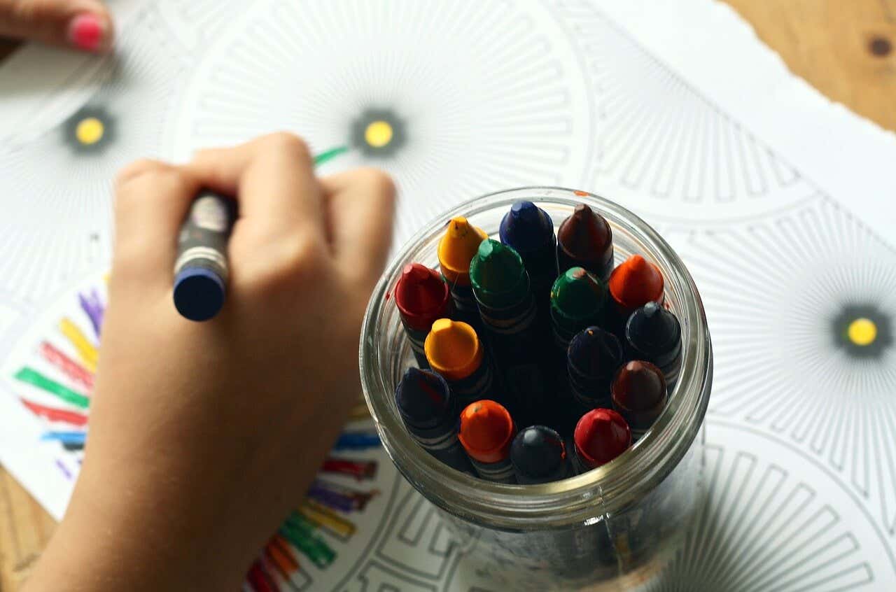 Mano de un niño dibujando y pinturas de colores para aprovechar todos los beneficios de dibujar.
