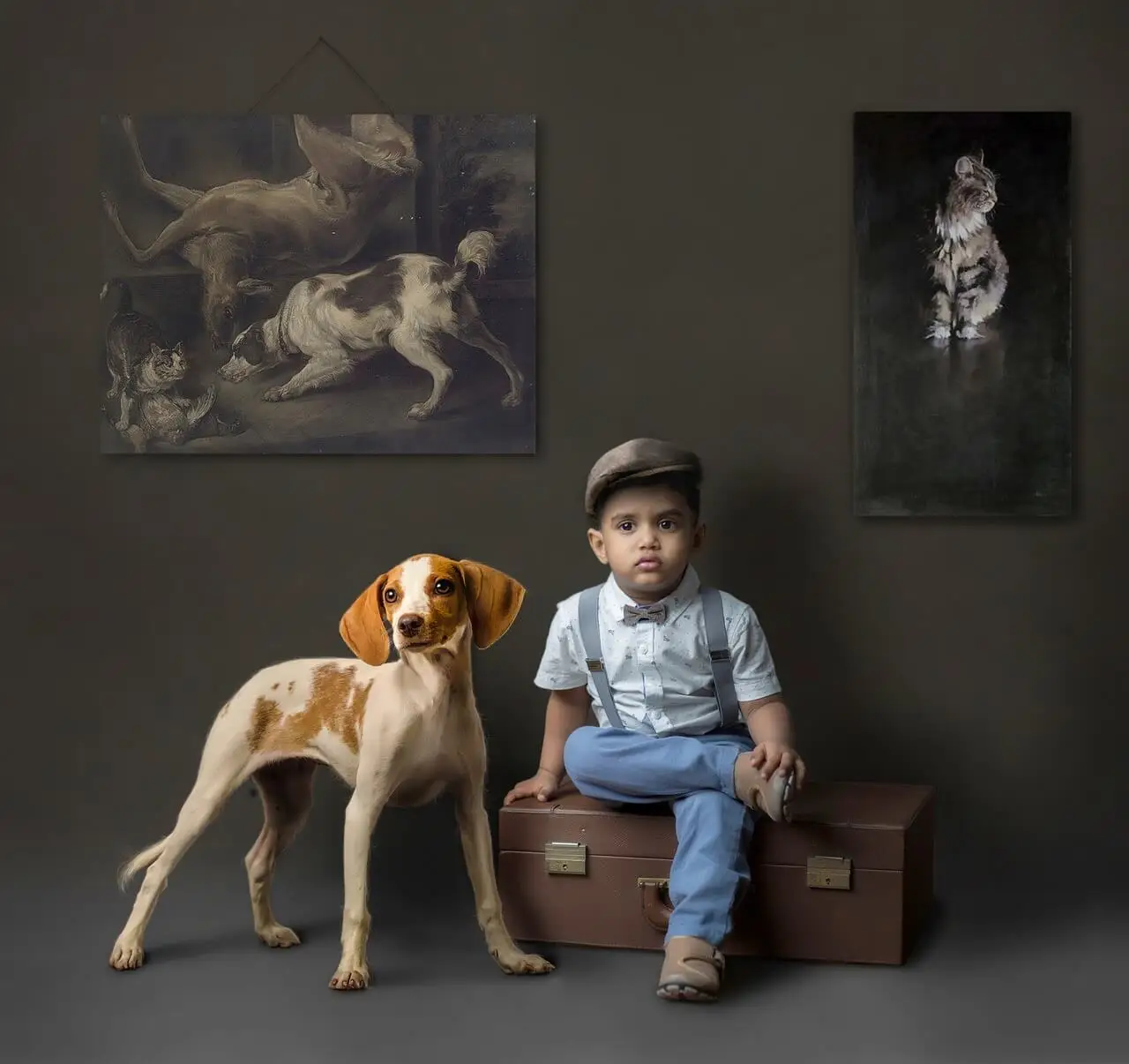 Niño sentado en una maleta acompañado de un perro con fondo oscuro y cuadros de animales.