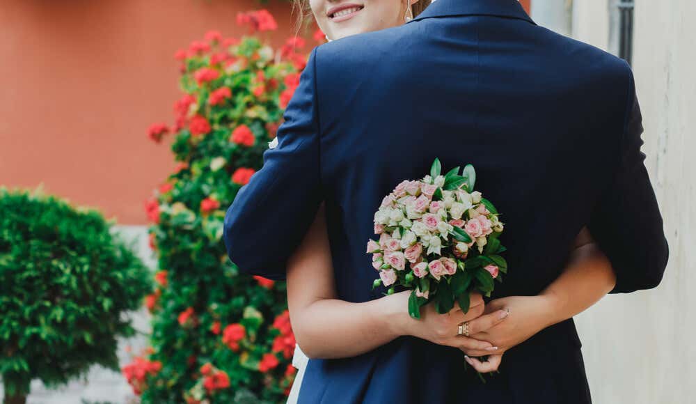 Pareja de novios recién casados abrazándose con un ramo de flores en la mano.