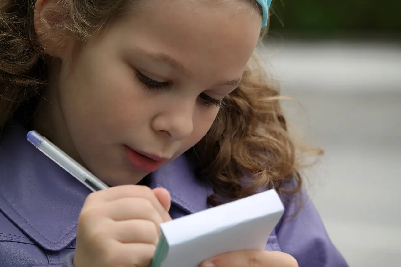 Niña escribiendo con bolígrafo en una libreta.