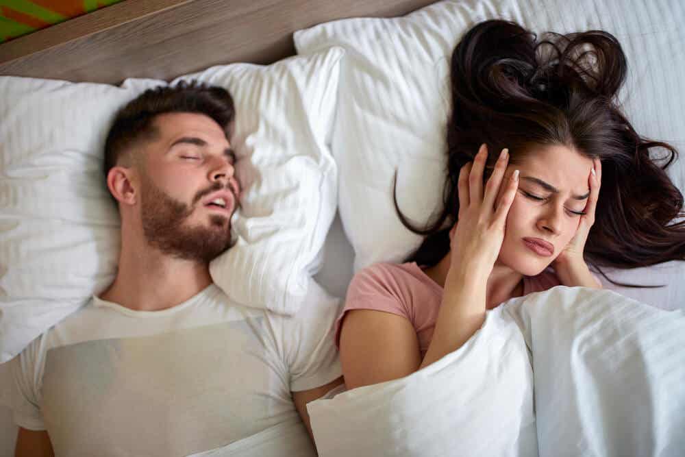 Mujer tapándose los oídos en la cama ante los ronquidos de la pareja.