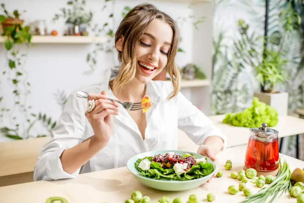 Chica sonriente comiéndose una ensalada.