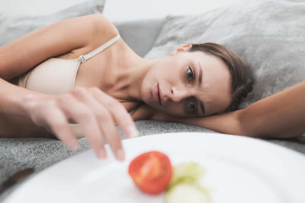 Mujer con anorexia junto a un plato de comida casi vacío.