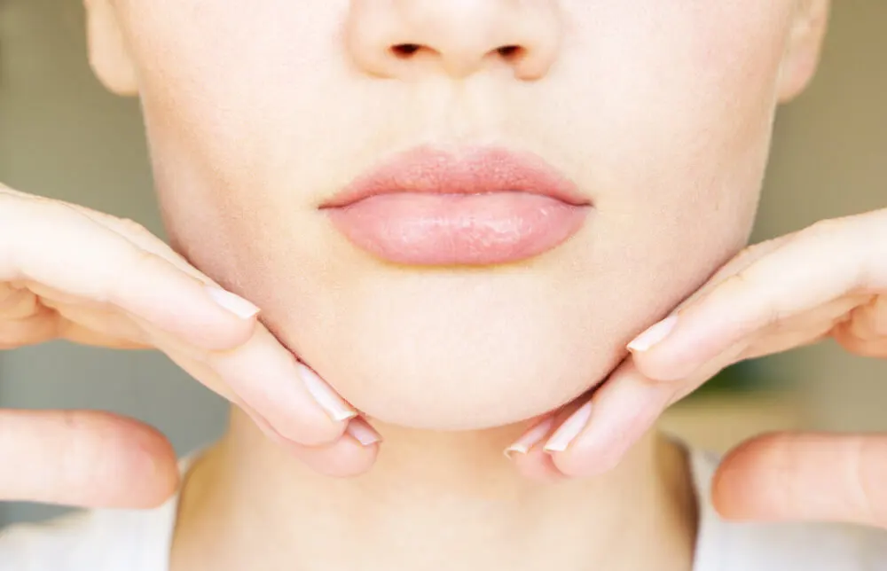 Mujer tocándose la barbilla con unos labios voluptuosos.