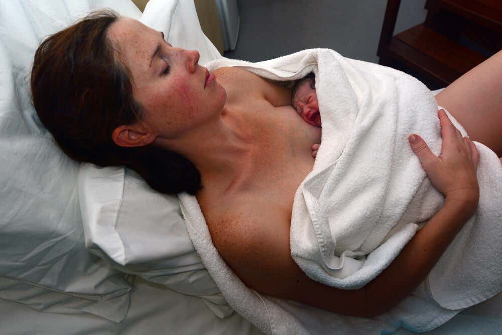 Mujer acostada junto a su hijo recién nacido.