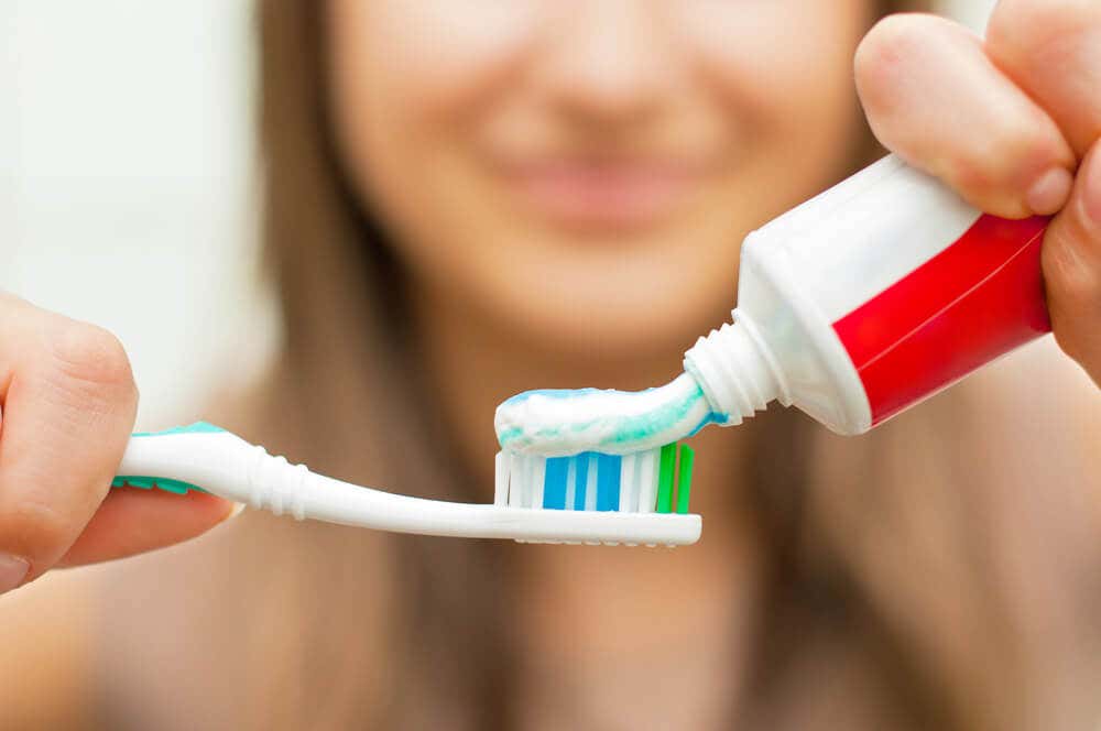 Mujer echando pasta de dientes en el cepillo.