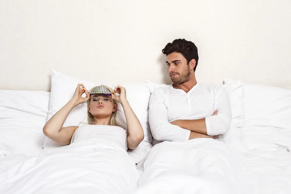 Pareja en la cama. Mujer preparada para dormir, hombre despierto.