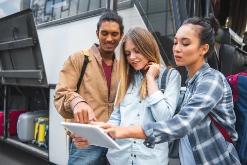 Grupo de amigos al lado de un autobus mirando una tablet.