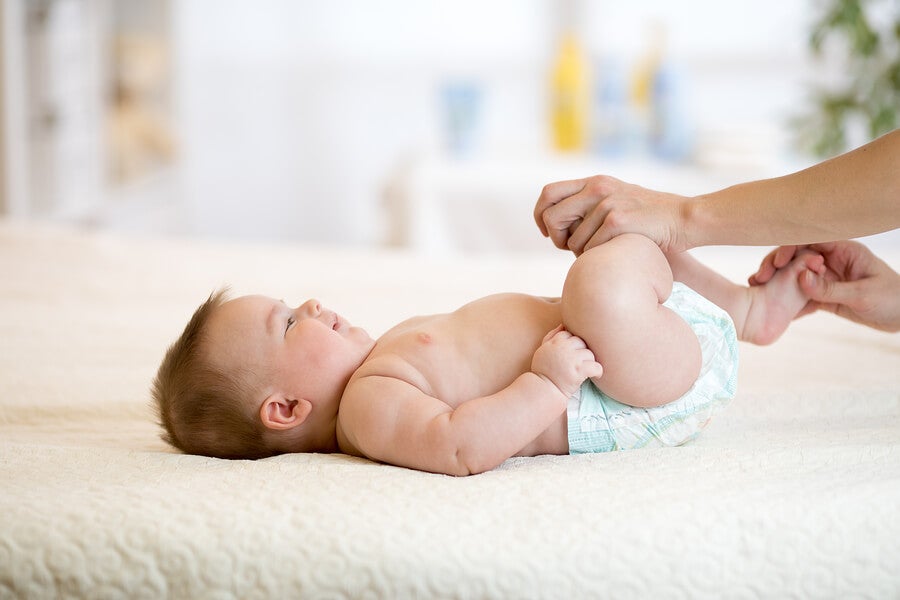 Bebé tumbado boca arriba mueve las piernas con ayuda de un adulto.