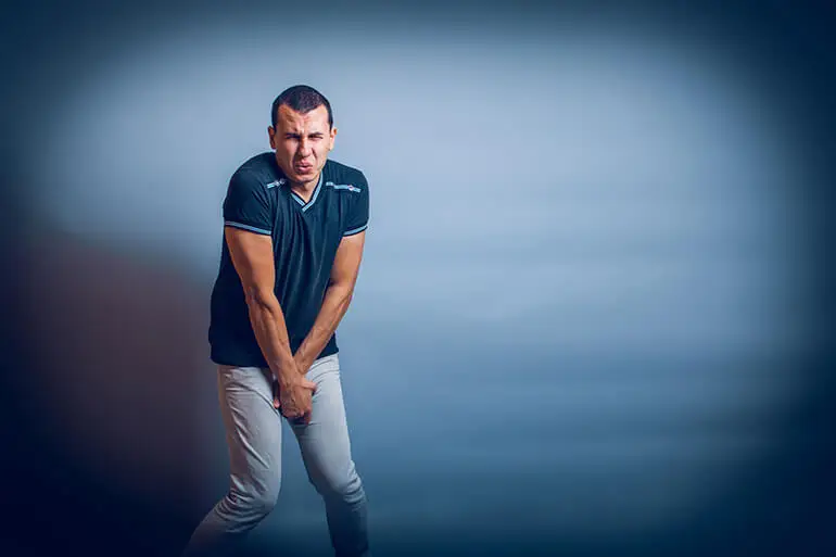 Hombre con expresión de dolor y las manos en el pubis