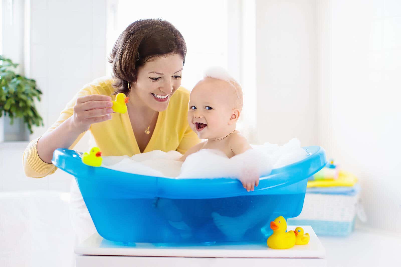 Bebé jugando en la bañera supervisado por su mamá.
