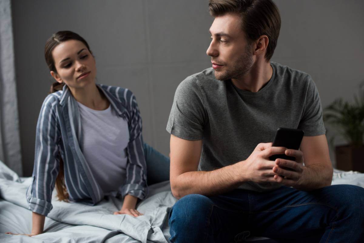 Mujer en la cama y hombre viendo el móvil