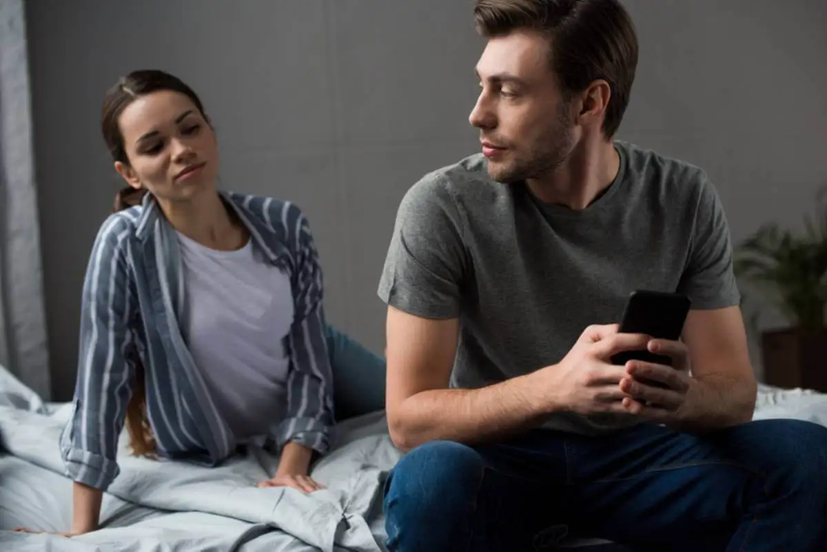 Mujer en la cama y hombre viendo el móvil
