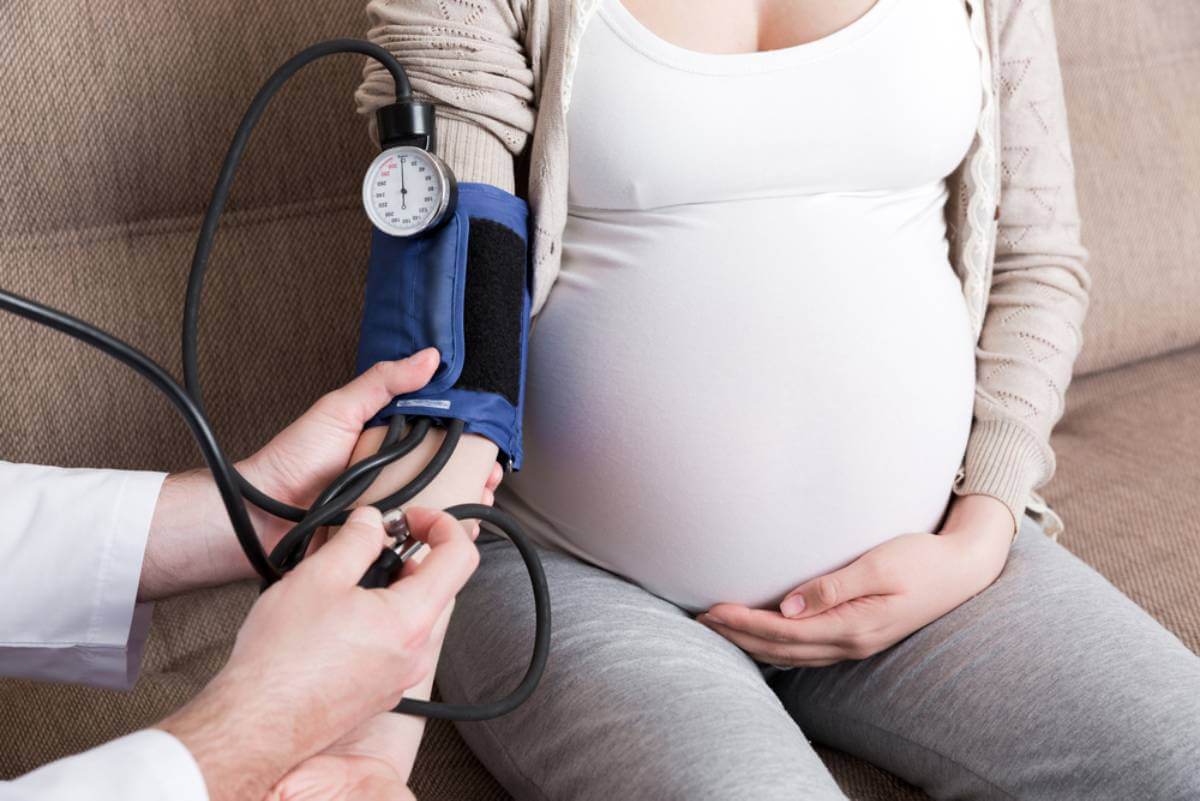 Mujer embarazada midiéndose la presión arterial: factores que pueden causar un parto prematuro