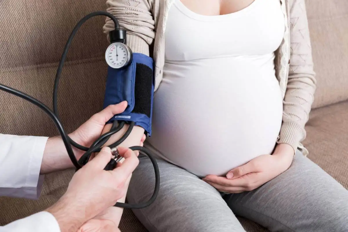 Mujer embarazada midiéndose la presión arterial: factores que pueden causar un parto prematuro