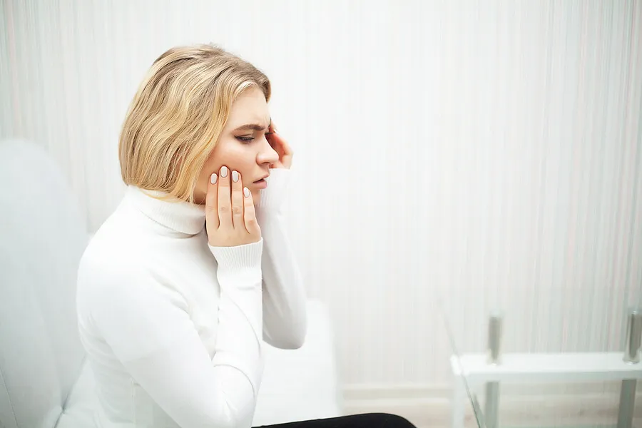 Mujer rubia que toca la mejilla porque tiene un dolor dental