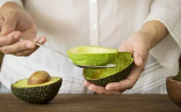 Persona sacándole la pulpa al aguacate.