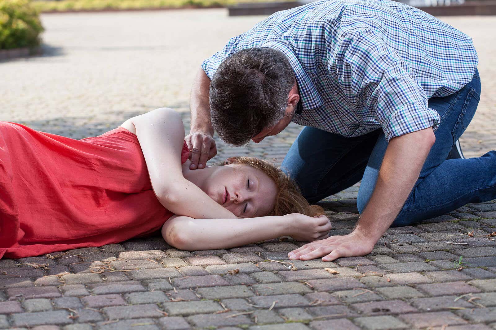 Hombre comprobando pulso de la chica desmayada en la calle.